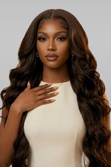 Woman with long, wavy brown hair wearing a white top against a gray background