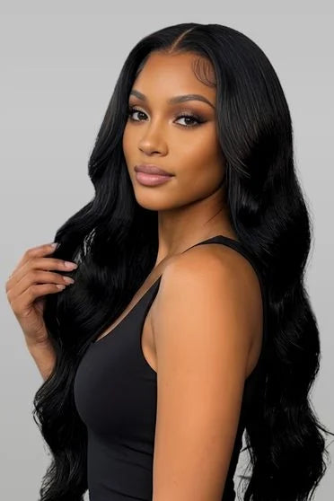 Woman with long, wavy black hair wearing a black sleeveless top against a gray background